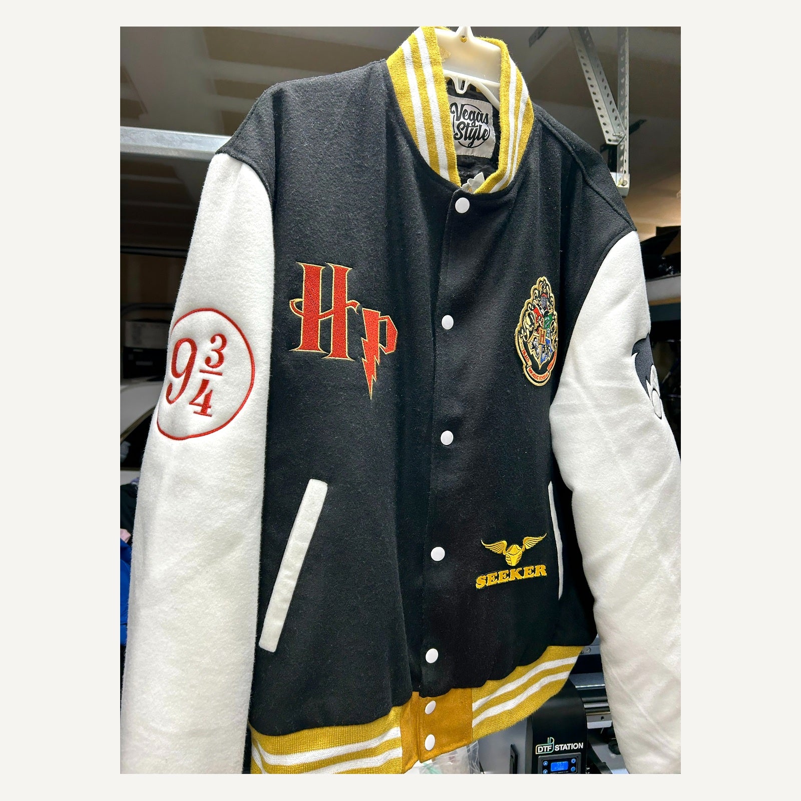 Angled front detail of black cream and gold Harry Potter-themed varsity jacket